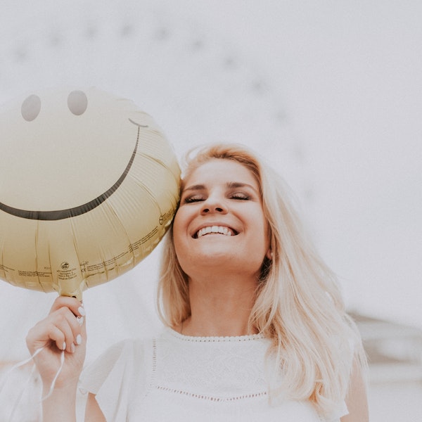 Foto com uma mulher sorrindo segurando um balão com o emoji de um sorriso para ilustrar matéria sobre seguro de vida para mulher